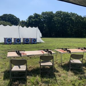 Crossbow range with 4 crossbows on tables in a field with a large net and 4 targets.