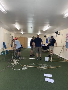 5 adults in a room with a green floor looking at mini pioneering activities